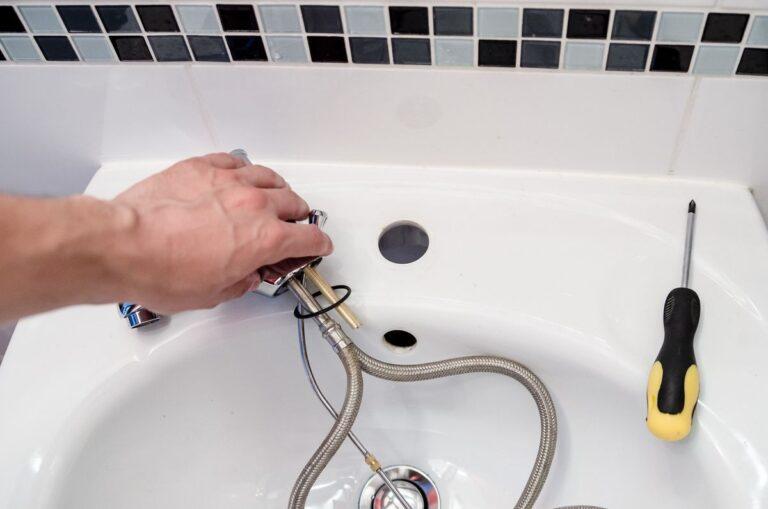 main démontant un robinet de lavabo avec flexibles de plomberie